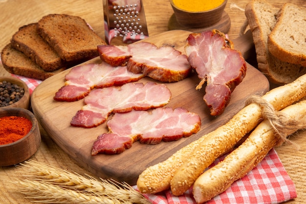 Vue de dessous des tranches de becon sur une planche à découper du poivre rouge et noir dans de petits bols du pain brun et blanc sur une table en bois