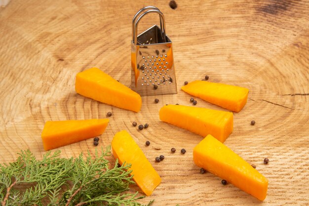 Vue de dessous tranches de fromage éparpillés poivre noir boîte râpe branche de pin sur table en bois