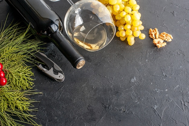 Vue de dessous verre à vin raisins jaunes frais bouteille de vin noyer baies rouges de noël sur table noire copie place