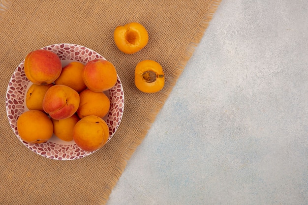 Photo gratuite vue de dessus des abricots dans un bol et couper la moitié un sur un sac sur fond blanc avec copie espace