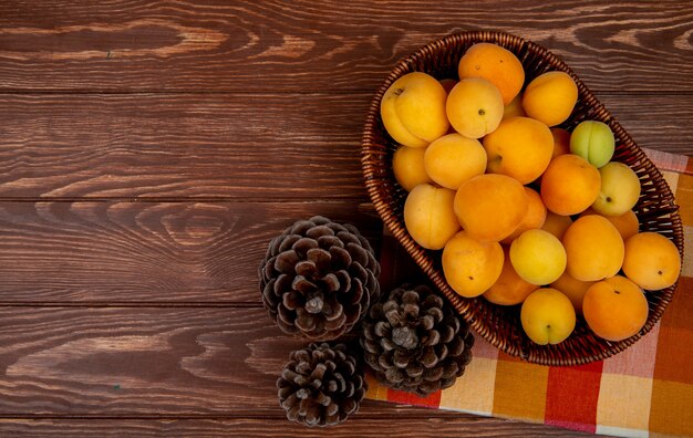 Vue de dessus des abricots dans le panier sur le tissu avec des pommes de pin sur fond de bois avec copie espace