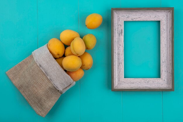 Vue de dessus des abricots dans un sac de jute avec un cadre gris sur une surface bleue