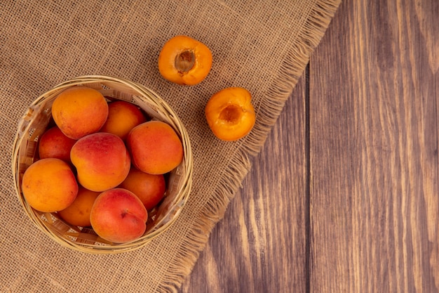 Vue de dessus des abricots entiers dans le panier et couper la moitié un sur un sac sur fond de bois avec espace copie