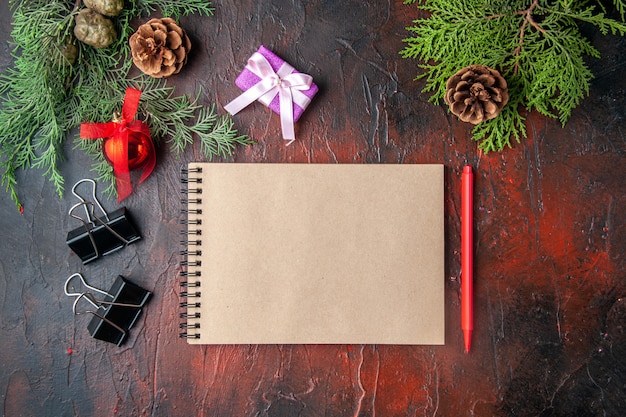 Vue de dessus des accessoires de décoration de branches de sapin et cadeau à côté d'un cahier avec un stylo sur fond sombre