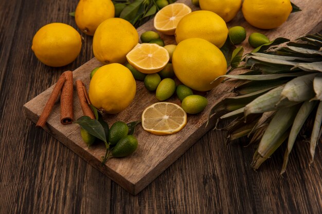 Vue de dessus des agrumes tels que les kinkans et les citrons avec des bâtons de cannelle sur une planche de cuisine en bois avec des ananas sur un fond en bois