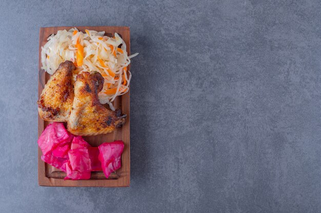 Vue de dessus des ailes de poulet grillées et des choux en conserve sur planche de bois.