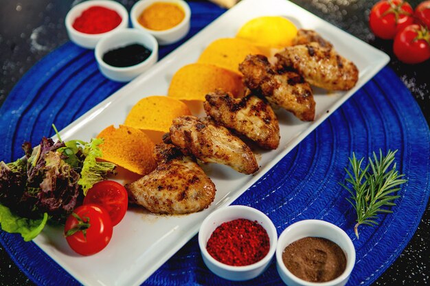 Vue de dessus des ailes de poulet grillées servies avec pommes de terre frites et salade fraîche