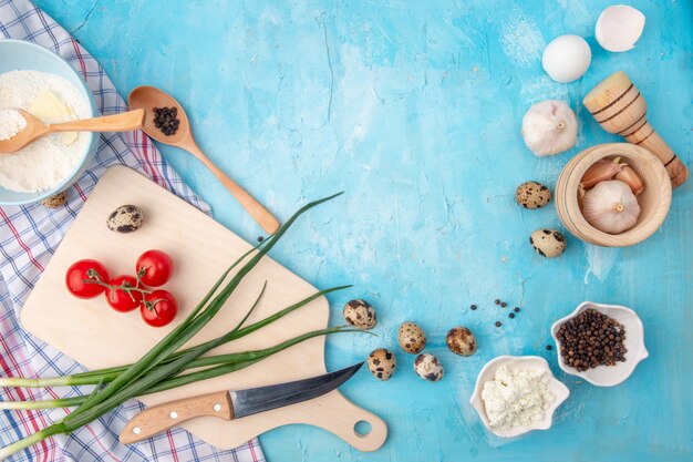 Vue de dessus des aliments comme l'ail d'œuf d'échalote tomate et d'autres avec un couteau et une planche à découper sur fond bleu avec copie espace