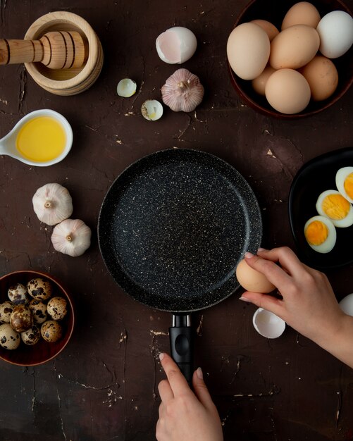 Vue de dessus des aliments sous forme d'œuf à l'ail au beurre avec poêle et oeuf de freinage à la main de femme sur fond marron