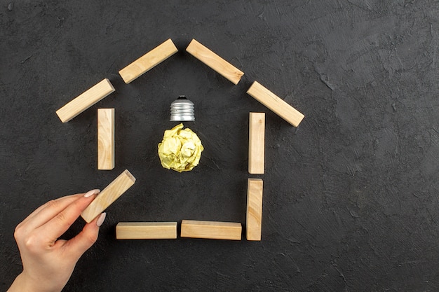 Photo gratuite vue de dessus de l'ampoule idealight dans des blocs de bois en forme de maison bloc de bois dans une main féminine sur fond noir