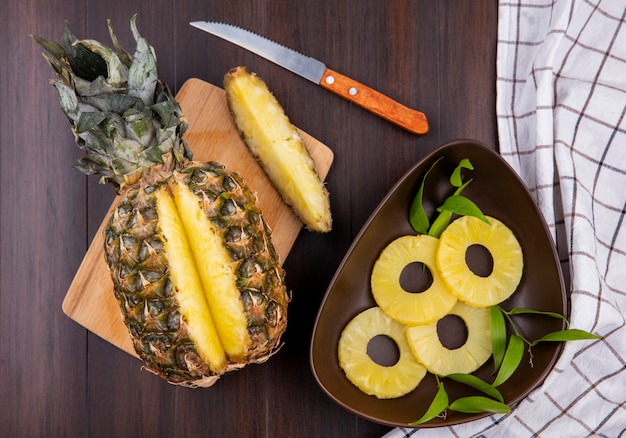 Photo gratuite vue de dessus de l'ananas avec une pièce découpée dans des fruits entiers sur une planche à découper avec des tranches d'ananas et un couteau sur une surface en bois