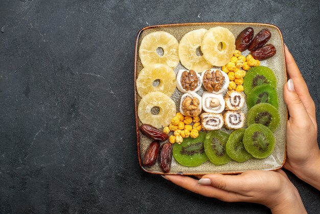 Vue de dessus anneaux d'ananas de fruits secs en tranches et kiwis aux noix sur bureau gris raisin sec fruits secs santé vitamine douce