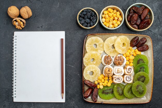 Vue de dessus anneaux d'ananas de fruits secs en tranches et kiwis sur bureau gris fruits secs raisins secs vitamine aigre santé