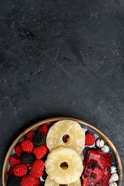 Photo gratuite vue de dessus des anneaux d'ananas séchés avec des baies de confiture sur un bureau gris