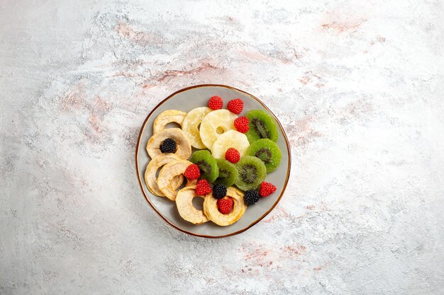 Vue de dessus des anneaux d'ananas séchés avec des kiwis et des pommes séchés sur une surface blanche