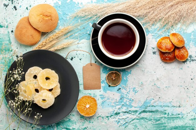 Vue de dessus anneaux d'ananas séchés avec tasse de thé sur le gâteau de bureau bleu cuire au four biscuit aux fruits biscuits au sucre sucré