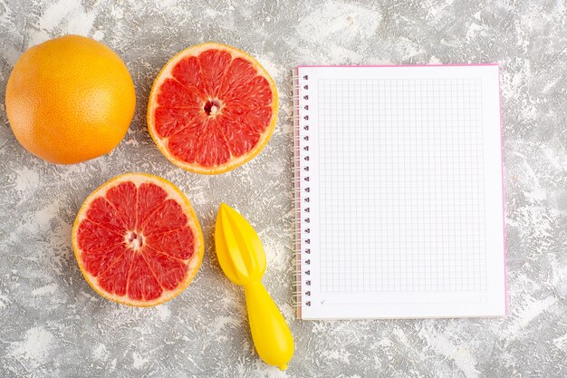 Vue de dessus des anneaux de pamplemousse frais avec bloc-notes sur la surface blanche claire