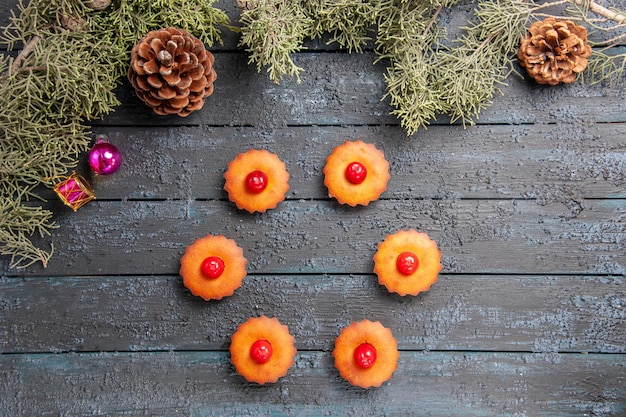 Vue de dessus arrondi cupcakes cerise branches de sapin jouets de Noël et cônes sur un sol en bois foncé avec espace de copie