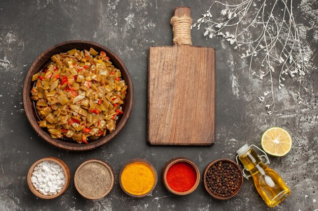 Vue de dessus assiette appétissante de haricots verts et de tomates à côté de la planche à découper en bois épices colorées citron et bouteille d'huile sur la table