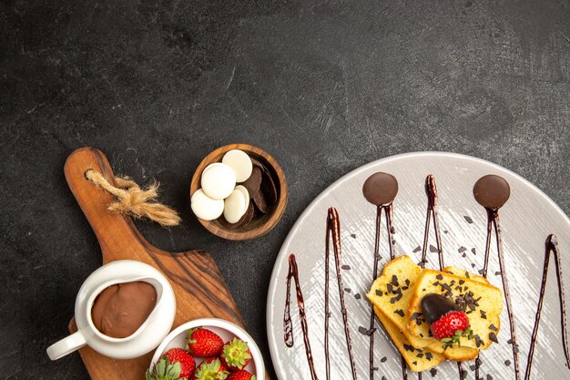 Photo gratuite vue de dessus assiette de baies de gâteau au chocolat et de fraises à côté des bols de chocolat et de fraises sur le plateau de la cuisine