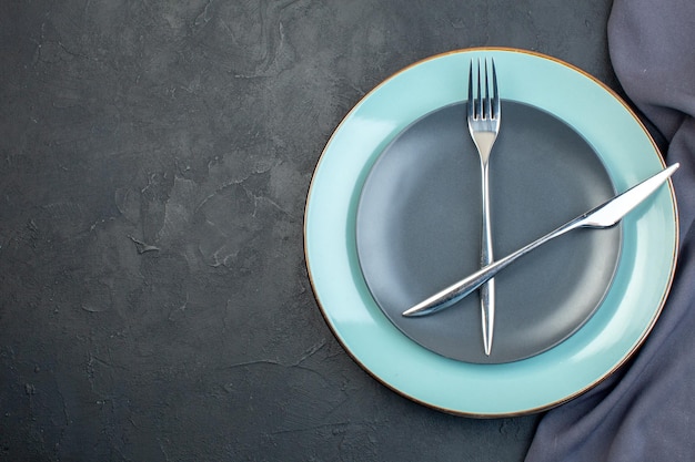 Vue de dessus assiette bleue avec assiette grise fourchette et couteau sur fond sombre argenterie féminité colorée faim dames grace diner