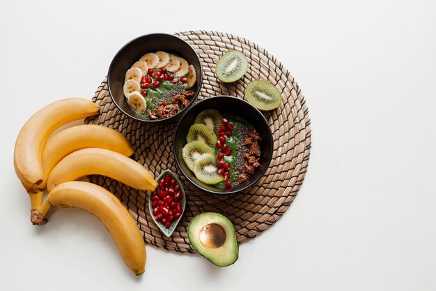 Vue de dessus sur une assiette de bol de smoothie vert garni d'avocat et d'épinards, de graines de grenade et de granola.