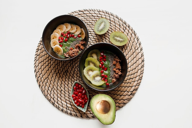 Vue de dessus sur une assiette de bol de smoothie vert garni d'avocat et d'épinards, de graines de grenade et de granola.