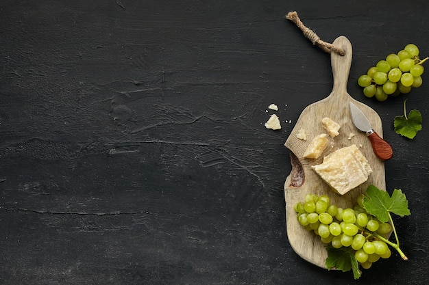 Photo gratuite vue de dessus d'une assiette de fromage savoureux avec des fruits, du raisin sur une assiette de cuisine en bois sur le fond de pierre noire