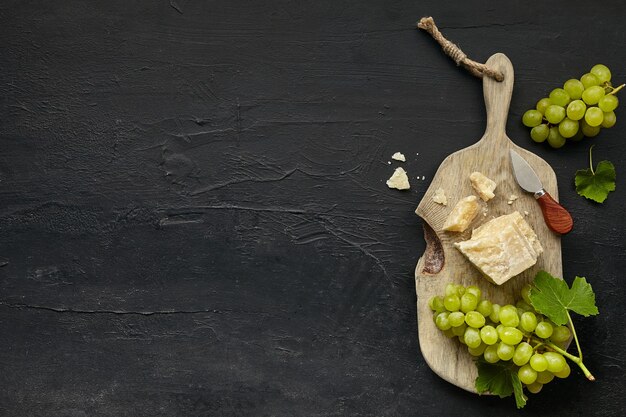 Vue de dessus d'une assiette de fromage savoureux avec des fruits, du raisin sur une assiette de cuisine en bois sur le fond de pierre noire