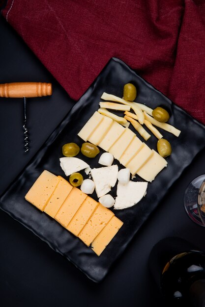 Vue de dessus de l'assiette de fromages comme parmesan et cheddar avec olive et tire-bouchon avec chiffon sur tableau noir