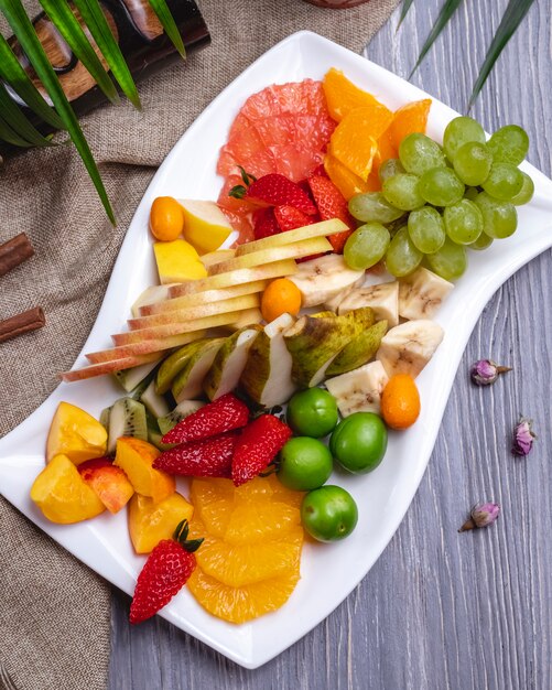 Vue de dessus assiette de fruits orange fraise banane kiwi poire raisins et cerise prune