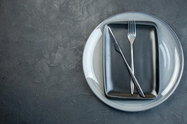 Vue de dessus assiette noire avec couteau à fourchette et assiette grise sur fond sombre argenterie diner coloré féminité faim grâce couverts