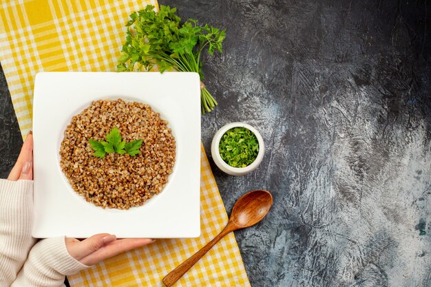 Vue de dessus d'une assiette de sarrasin cuit savoureux avec des verts sur une table gris clair