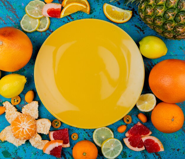 Vue de dessus de l'assiette vide avec pamplemousse mandarine ananas citron kumquat autour sur fond bleu