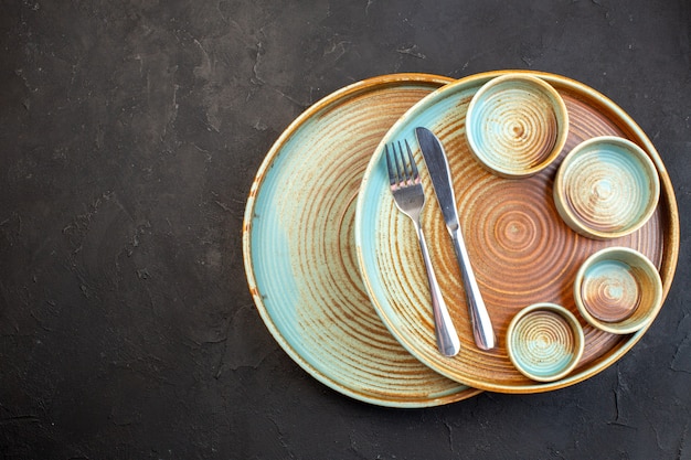 Photo gratuite vue de dessus assiettes brunes avec fourchette et couteau sur une surface sombre