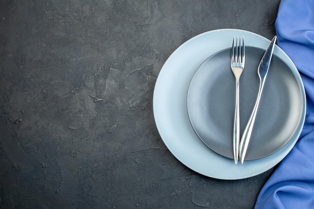 Vue de dessus des assiettes élégantes avec fourchette et couteau sur fond sombre grâce à l'argenterie colorée du dîner de la faim