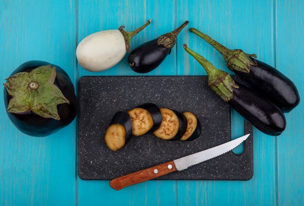 Vue de dessus aubergine noire tranchée sur une planche à découper avec un couteau et ensemble sur fond turquoise