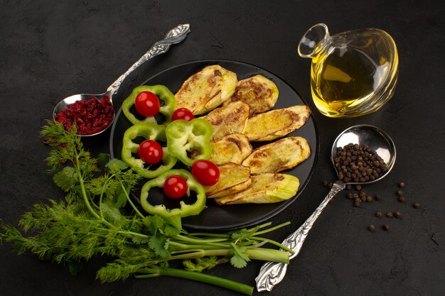 Vue de dessus d'aubergines cuites tranchées à l'intérieur de la plaque noire avec des légumes frais sur le sol sombre