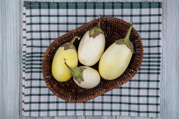 Photo gratuite vue de dessus d'aubergines jaunes et blanches dans le panier sur tissu à carreaux sur fond de bois