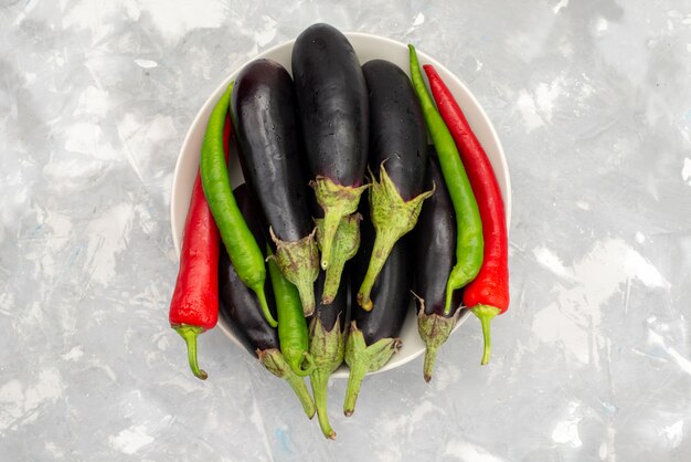 Vue de dessus aubergines noires crues avec des poivrons sur le bureau lumineux repas alimentaire légumes épices