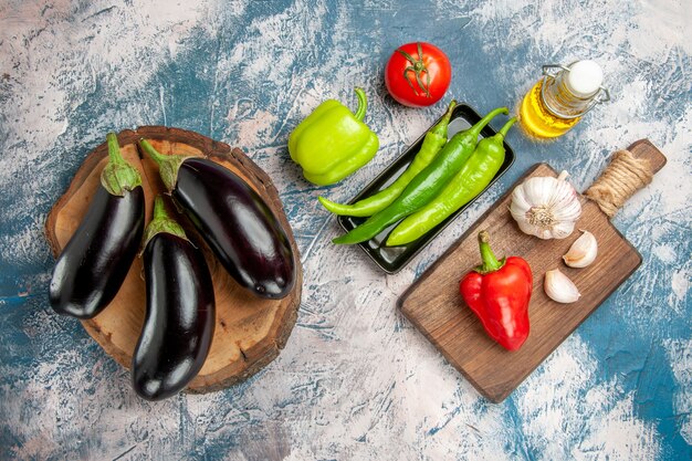 Vue de dessus aubergines sur planche de bois d'arbre piments forts sur plaque noire sur planche à découper huile d'aubergine sur fond bleu-blanc