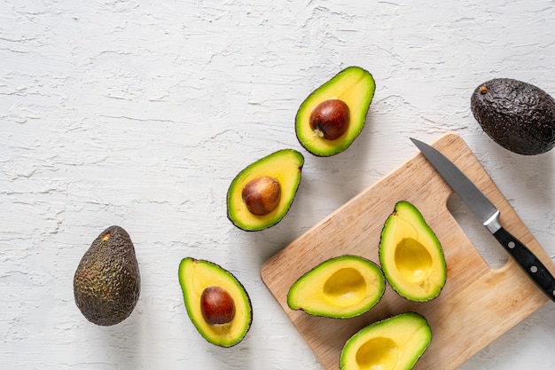 Vue de dessus des avocats frais coupés en deux sur une surface blanche, avec une planche à découper et un couteau, espace copie