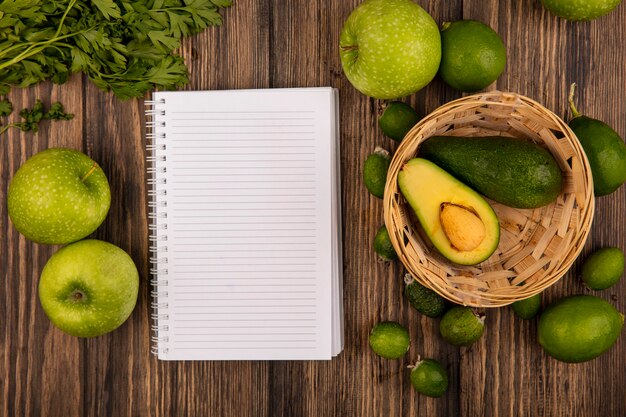 Vue de dessus des avocats frais sur un seau avec des pommes vertes limes feijoas et persil isolé sur un fond en bois avec espace copie