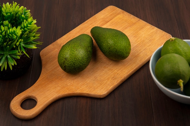 Vue de dessus des avocats verts frais sur une planche de cuisine en bois avec des limes sur un bol sur un mur en bois