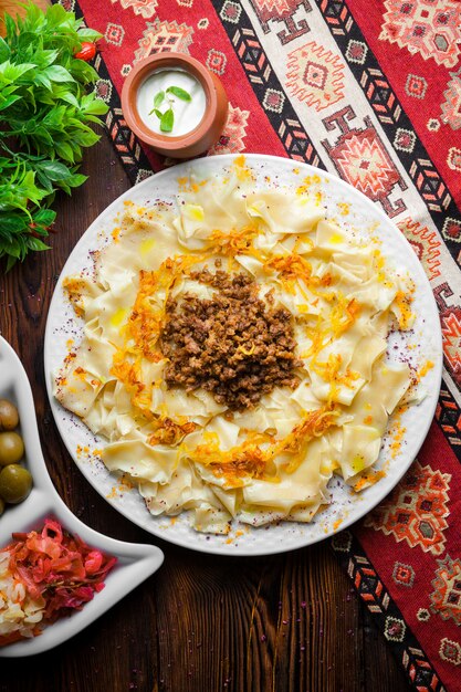 Vue de dessus azerbaijani guru khingal pâtes caucasiennes avec viande hachée frite et oignon avec sauce à la crème sure et cornichons sur une nappe verticale