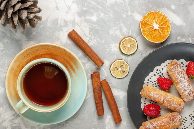 Vue de dessus des bagels en poudre de sucre avec des fraises et une tasse de thé sur une surface blanche