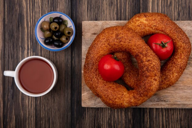 Vue de dessus des bagels turcs sur une planche de cuisine en bois avec des olives sur un bol avec une tasse de thé sur un fond en bois