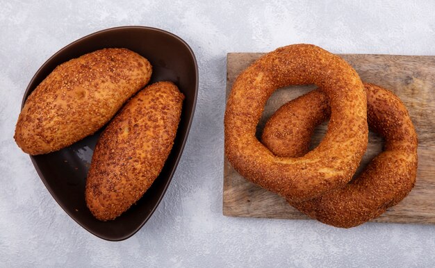 Vue de dessus des bagels turcs traditionnels sur une planche de cuisine en bois avec galettes de sésame sur un bol brun sur fond blanc