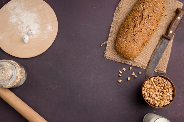 Vue de dessus de la baguette et du couteau sur un sac avec des cors et des flocons d'avoine et de la farine sur une planche à découper sur fond marron avec copie espace