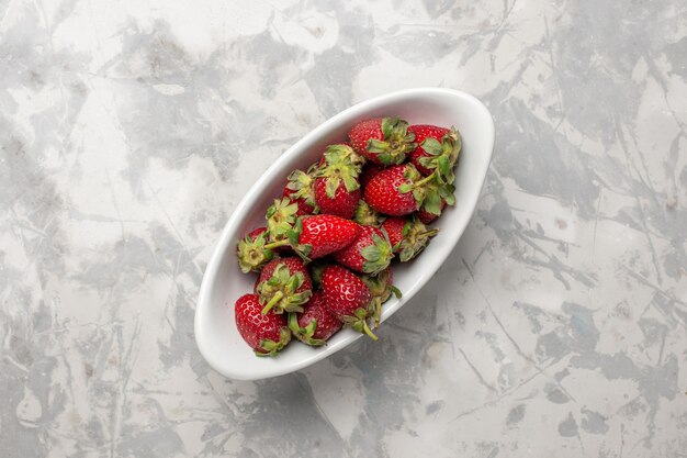 Vue de dessus les baies de fraises rouges fraîches à l'intérieur de la plaque sur la surface blanche berry fruit plante fraîcheur